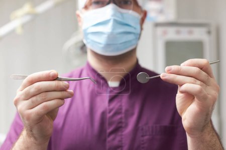 Photo for Selective focus on a sterile stainless steel dental mirror and probe in the hands of a male dentist doctor, ready for performing to a patient a dental check-up and teeth treatment. Dentistry. Medicine - Royalty Free Image