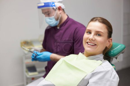 Photo for Portrait of happy female patient in dentist's chair, smiling with beautiful toothy smile during a dental check-up in a modern dentistry clinic. Pretty woman receiving teeth treatment. Dental practice - Royalty Free Image