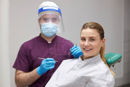 Photo for Young charming woman smiling a beautiful smile at camera, sitting at dentist chair, ready for dental check-up in a dentistry clinic. Prophylaxis teeth treatment. Dental health and oral hygiene concept - Royalty Free Image