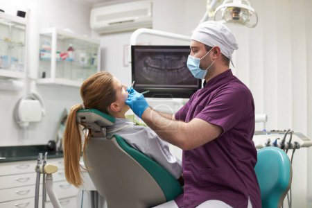 Photo for Doctor dentist orthodontist conducting an examination of the oral cavity of a female patient on a dental chair, according to the treatment needs to do after analyzing the X-ray dental panoramic film - Royalty Free Image