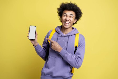 Téléchargez les photos : Portrait d'un homme afro-américain souriant tenant un téléphone portable faisant des achats en ligne pointant du doigt l'écran vide isolé sur fond jaune. Homme heureux moderne utilisant l'application mobile, commander de la nourriture. Maquette - en image libre de droit
