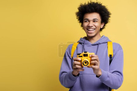 Photo for Smiling photographer holding photo camera isolated on yellow background, copy space. Travel concept - Royalty Free Image
