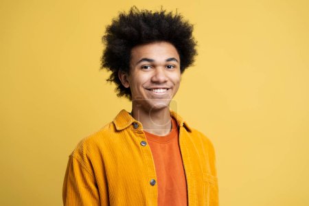 Téléchargez les photos : Portrait d'homme afro-américain souriant confiant aux cheveux bouclés portant des vêtements décontractés élégants isolés sur fond jaune. Joyeux étudiant qui regarde la caméra. Concept d'éducation - en image libre de droit