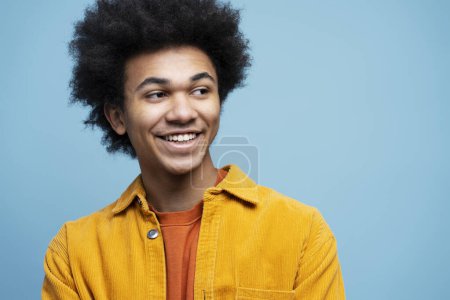 Téléchargez les photos : Homme afro-américain souriant aux cheveux bouclés, portant des vêtements décontractés isolés sur fond bleu - en image libre de droit