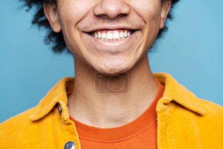 Photo for Closeup of young African American man with toothy smile isolated on blue background. Health care, dental treatment, oral hygiene concept - Royalty Free Image