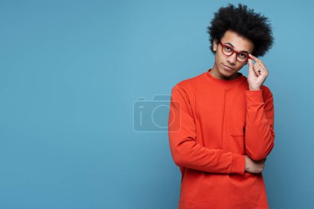 Foto de Portrait of smart pensive university student wearing stylish eyeglasses looking at camera isolated on blue background, copy space. Education concept - Imagen libre de derechos