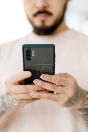 Photo for Closeup of asian man hands holding mobile phone shopping online, ordering food from home, selective focus. Handsome hipster with stylish tattooed hands reading text message. Technology concept - Royalty Free Image