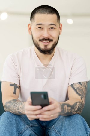 Photo for Portrait of smiling confident Asian businessman holding cellphone, communication, working online, sitting in office. Smiling man using mobile app shopping online - Royalty Free Image