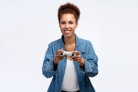 Téléchargez les photos : African American gamer woman jouer à un jeu vidéo en utilisant joystick sur fond blanc isolé. Femme heureuse excitée regardant vers la caméra - en image libre de droit