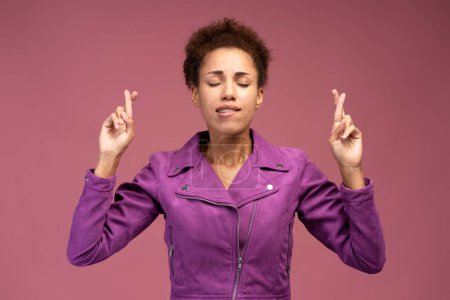 Téléchargez les photos : Hopeful nervous brown haired woman crossing fingers for luck, hope for better, ritual, looks up with hopeful look. Indoor studio shot isolated on pink background - en image libre de droit