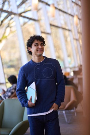 Photo for Smiling Hispanic guy holding laptop, looking aside while visiting library. Smart student coming to the library campus, making researches, preparing exams, searching informations for diploma project - Royalty Free Image