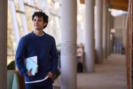 Foto de Retrato seguro de un joven estudiante latinoamericano joven y sonriente que visita una biblioteca moderna. Gente. Educación. Erudición. Aprendiendo. Conocimiento - Imagen libre de derechos