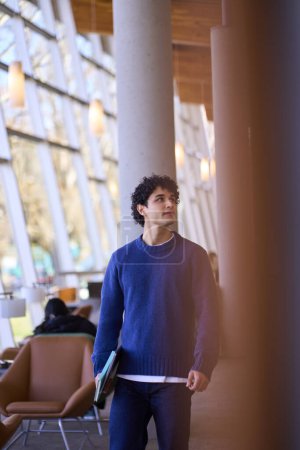 Photo for Confident Latin American young man, a university student, with laptop and notepad, visiting a modern library campus. Back to school concept. People. Education. Erudition. Learning. Knowledge - Royalty Free Image