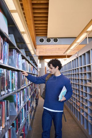 Photo for Smart Latin American male student, standing by bookshelves in university library campus and choosing books, searching informations for hi diploma project. Learning. Education. Educated people concept - Royalty Free Image