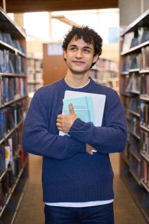 Photo for Positive male student thoughtfully looking aside at shelves with books, choosing interesting literature in bookstore. Happy Hispanic hipster young man having free time for enjoying hobby and learning - Royalty Free Image