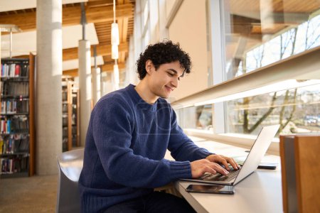 Photo for Smart Hispanic male student sitting at desk and using laptop, preparing diploma project in library campus. People. Education. Modern wireless technology. E-learning and distance communication concept - Royalty Free Image