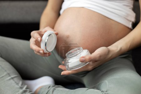 Photo for Close up of pregnant woman hand holding jar with moisturizer cream from stretch marks. Pregnancy, skin care product - Royalty Free Image