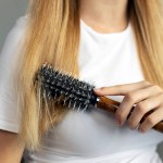 Closeup of woman hand brushing her hair at home, selective focus. Beauty and hair care concept