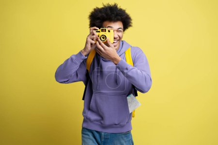 Photo for Young smiling African American photographer taking pictures isolated on yellow background. Portrait of happy attractive tourist holding photo camera. Vacation, travel concept - Royalty Free Image