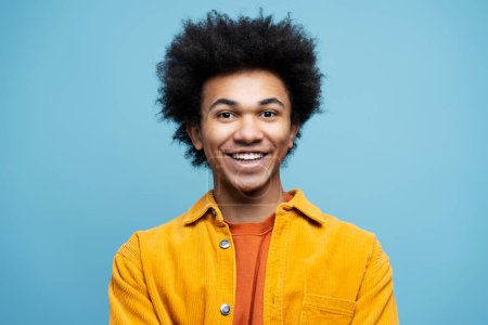 Foto de Retrato de hombre afroamericano sonriente y confiado con el pelo rizado usando ropa casual con estilo aislado sobre fondo azul. Feliz estudiante exitoso mirando la cámara. Concepto educativo - Imagen libre de derechos