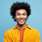 Portrait of confident smiling African American man with curly hair wearing stylish casual clothing isolated on blue background. Happy successful student looking at camera. Education concept 