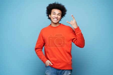 Photo for Young emotional African American man screaming, showing rock sign isolated on blue background. Music and having fun concept - Royalty Free Image