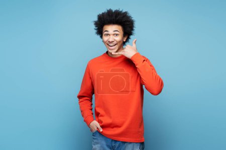 Photo for Laughing young African American man 20s wearing casual basic sweater doing phone gesture like says call me back isolated on blue colour wall background studio portrait - Royalty Free Image