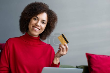 Foto de Mujer de negocios afroamericana sonriente sosteniendo la tarjeta de crédito usando el ordenador portátil, compras en línea, pidiendo comida en el sitio web. Feliz freelancer seguro de recibir pago. Tecnología, concepto de negocio exitoso - Imagen libre de derechos
