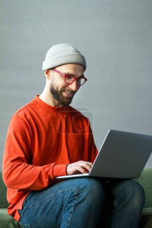 Photo for Portrait smiling successful man, programmer using laptop typing on keyboard working freelance project sitting at workplace. Modern bearded hipster watching training courses, planning startup in office - Royalty Free Image