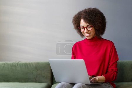 Foto de Mujer sonriente freelancer, copywriter escribiendo en el teclado, utilizando el ordenador portátil que trabaja en línea desde casa. Elegante mujer de negocios con gafas rojas planeando la puesta en marcha en la oficina moderna. Negocios exitosos - Imagen libre de derechos
