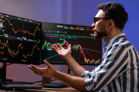 Frustrated man, crypto trader looking at computer monitor, working online with crypto chart sitting in modern office. Online trading concept