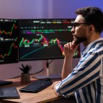 Serious trader looking at computer monitor, working online with crypto chart sitting in modern office