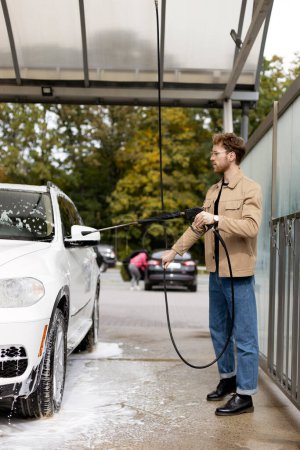 Foto de Suv blanco en auto-servicio de lavado de autos. Hombre atractivo lavando su coche, lavando espuma - Imagen libre de derechos