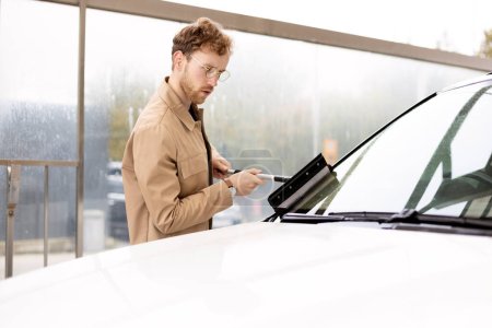 Photo for Serious man washing his car with window scraper at self-service station. Employee thoroughly wiping customer`s car. Car service concept - Royalty Free Image