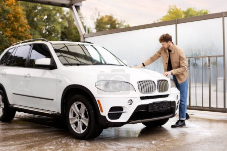 Téléchargez les photos : Travailleur masculin essuyant voiture avec chiffon en microfibre au lavage de voiture en plein air. - en image libre de droit