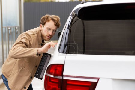Téléchargez les photos : Bel homme essuyant soigneusement voiture avec racleur de fenêtre. Concept de lave-auto libre-service - en image libre de droit