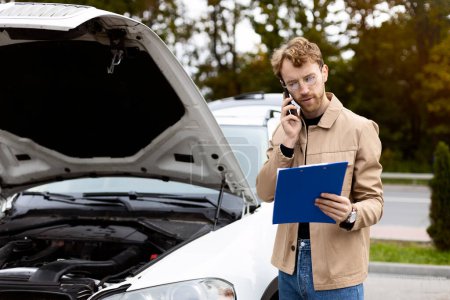 Photo for Serious man making diagnostic car, standing near open hood, talking on mobile phone. Car repair, concept - Royalty Free Image