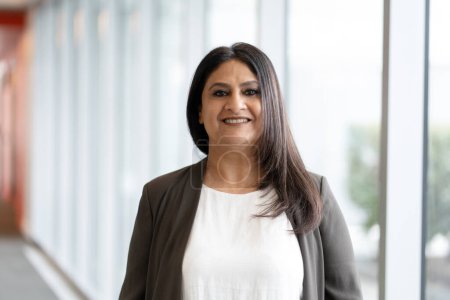 Téléchargez les photos : Portrait d'une femme d'affaires indienne souriante et confiante debout dans un bureau moderne. Heureux travailleur asiatique regardant la caméra à l'intérieur. Concept d'entreprise réussi - en image libre de droit