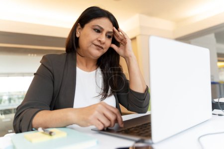 Photo for Stressed tired Indian businesswoman using laptop computer working project in office. Failure business. Serious freelancer missed deadline sitting at workplace - Royalty Free Image