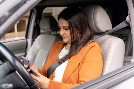 Photo for Confident multitasking mature female driver, businesswoman using smartphone, setting up navigator on mobile app, planning online meeting, sitting in driver's seat in car. People. Online communication - Royalty Free Image