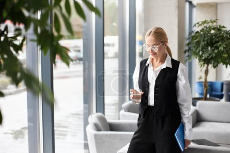 Téléchargez les photos : Belle femme d'affaires élégante tenant un verre d'eau debout dans un bureau moderne - en image libre de droit