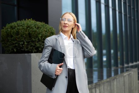 Photo for Portrait of attractive stylish business woman wearing eyeglasses, holding laptop, correct hair walking on the street - Royalty Free Image