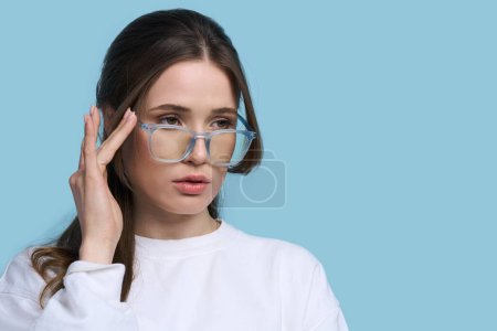 Photo for Caucasian young woman wearing stylish blue framed spectacles, looking at empty space for advertising text, isolated on blue background. Trendy eyeglasses. Eyesight. Vision. Fashion. Ophthalmology - Royalty Free Image