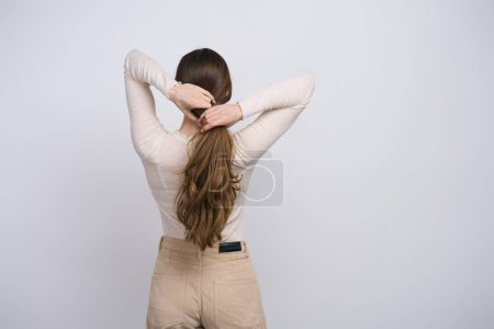 Photo for View from the back to a Caucasian young woman with strong healthy long shiny and silky hair, making a ponytail, isolated on white background with copy space. Fashion. Hair care and beauty concept - Royalty Free Image