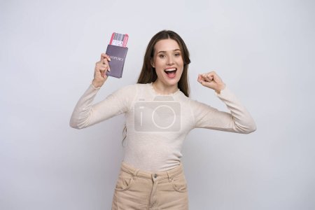 Photo for Excited Caucasian young woman holding passport and boarding pass, expressing happiness and positive emotions, going for weekend getaway, travelling abroad, smiling at camera, isolated white background - Royalty Free Image