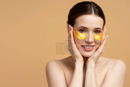 Téléchargez les photos : Belle femme caucasienne souriante utilisant des patchs dorés sous les yeux en regardant la caméra - en image libre de droit