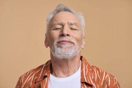 Photo for Closeup portrait of Caucasian handsome relaxed retired senior man in his 60s, smiling and posing with closed eyes over isolated beige background. Confident happy pensioner. People and holidays concept - Royalty Free Image