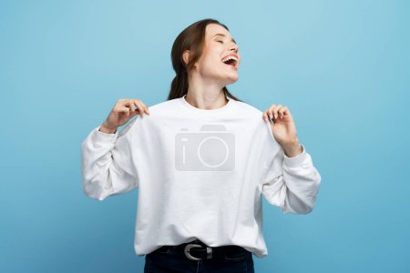 Foto de Joven mujer alegre vistiendo camisa blanca bailando y divirtiéndose aislada sobre fondo azul. Concepto de estilo de vida positivo - Imagen libre de derechos