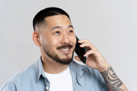 Photo for Portrait of handsome Asian man with tattoo talking on mobile phone, isolated on gray background. Successful businessman answering call, shopping, sales, communication - Royalty Free Image