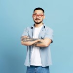 Smiling Asian man wearing stylish red eyeglasses and casual clothes isolated on blue background. Attractive male standing in studio with crossed arms, shopping, sale, advertising concept